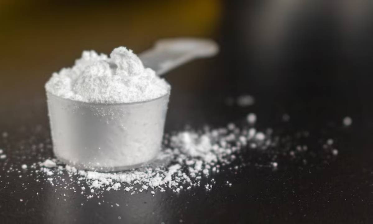 A clear measuring scoop filled with white powder sits on a dark surface, with some powder spilled around it.