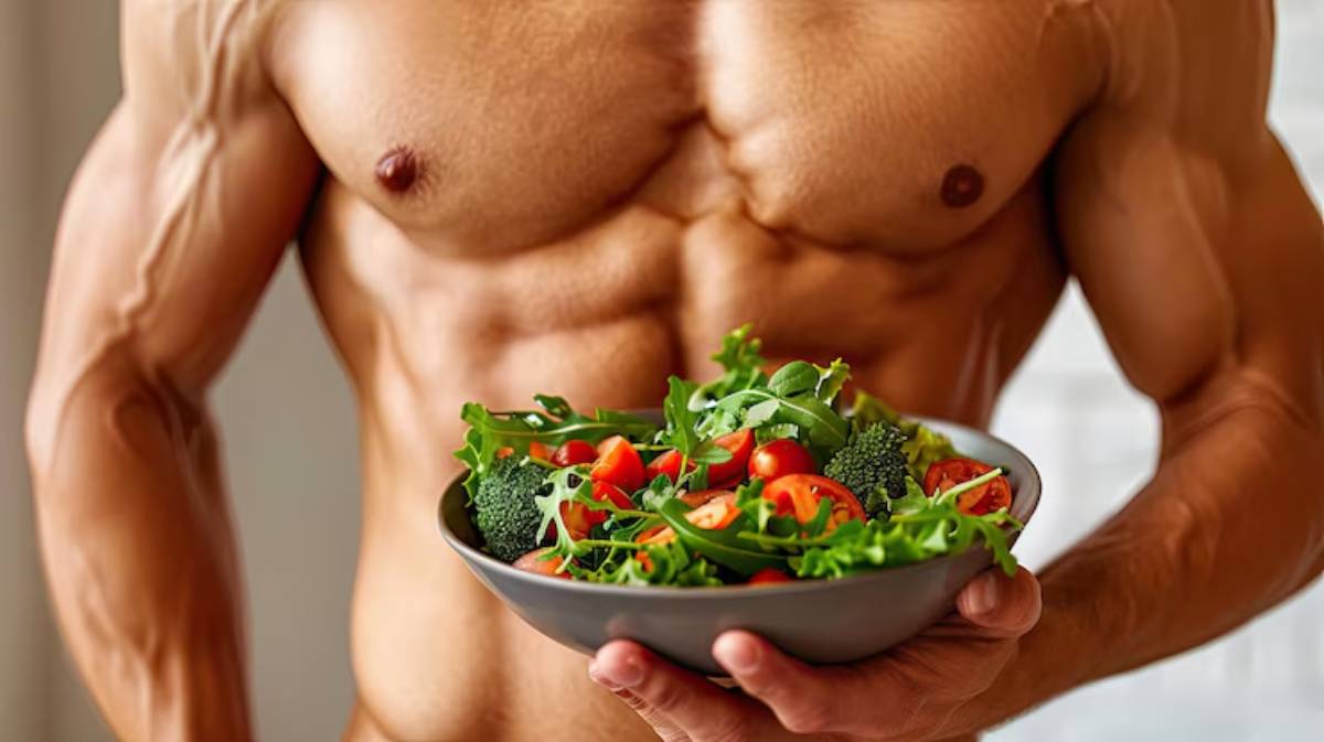 A muscular man holds a bowl of fresh salad, featuring leafy greens, cherry tomatoes, and broccoli, showcasing healthy eating.