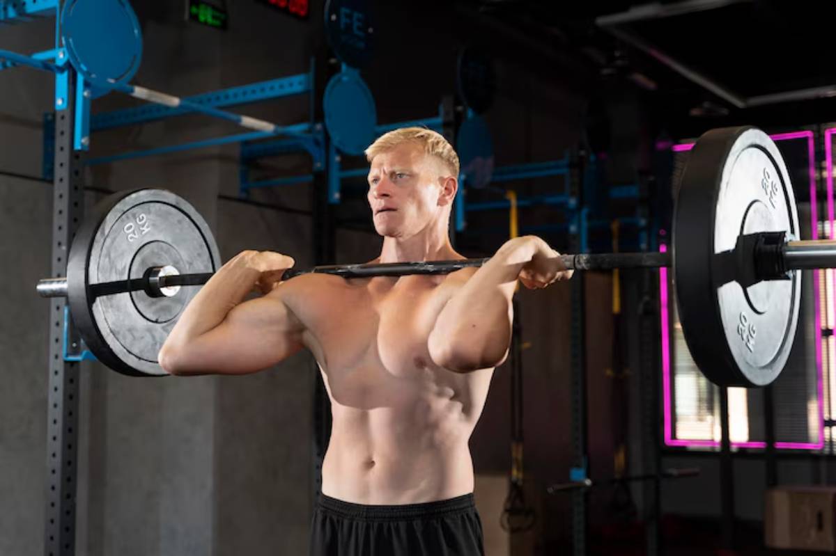 A muscular individual performs a barbell clean and press in a gym environment, emphasizing strength training and fitness.