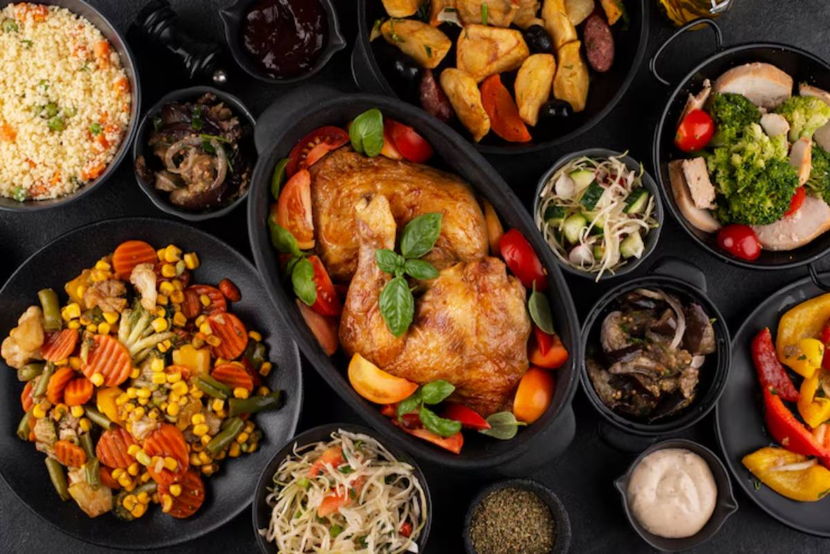 A vibrant spread of various dishes including roasted chicken, colorful vegetables, couscous, salads, and dipping sauces, arranged on dark plates.