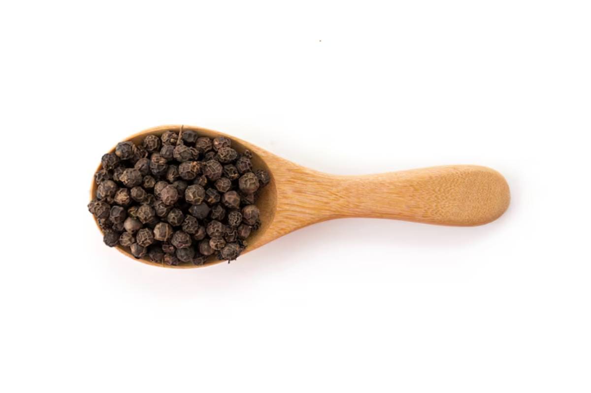 A wooden spoon filled with whole black peppercorns against a white background.