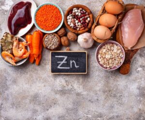 A variety of foods rich in zinc, including seafood, meats, vegetables, nuts, and grains, with a chalkboard displaying "Zn."