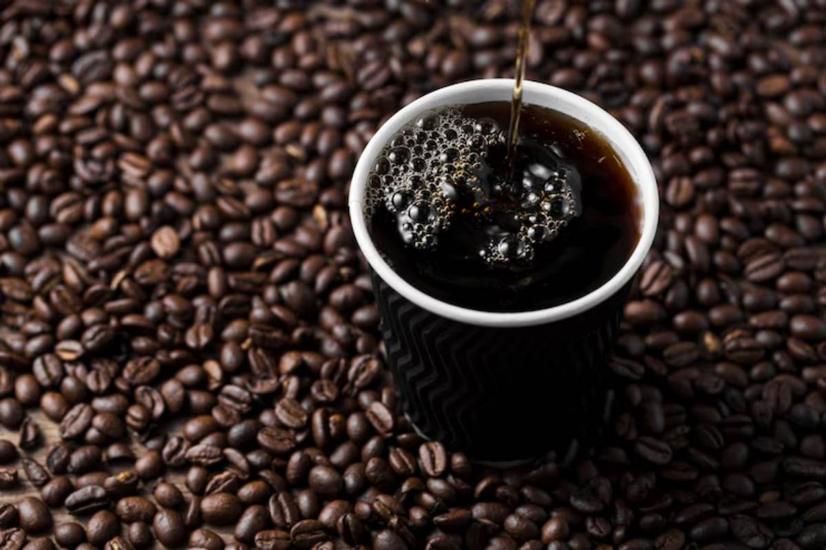 A black coffee cup filled with coffee sits on a white saucer, accompanied by scattered coffee beans on a clean white background.