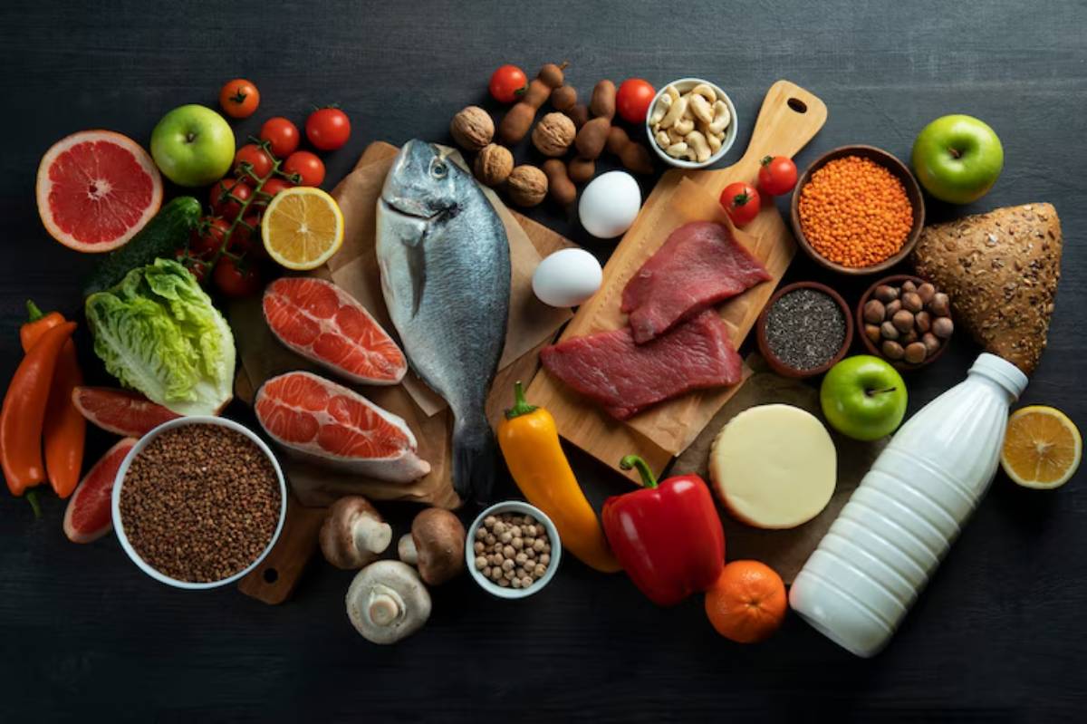 A colorful array of fresh foods including fish, meat, vegetables, fruits, nuts, and grains displayed on a wooden background.