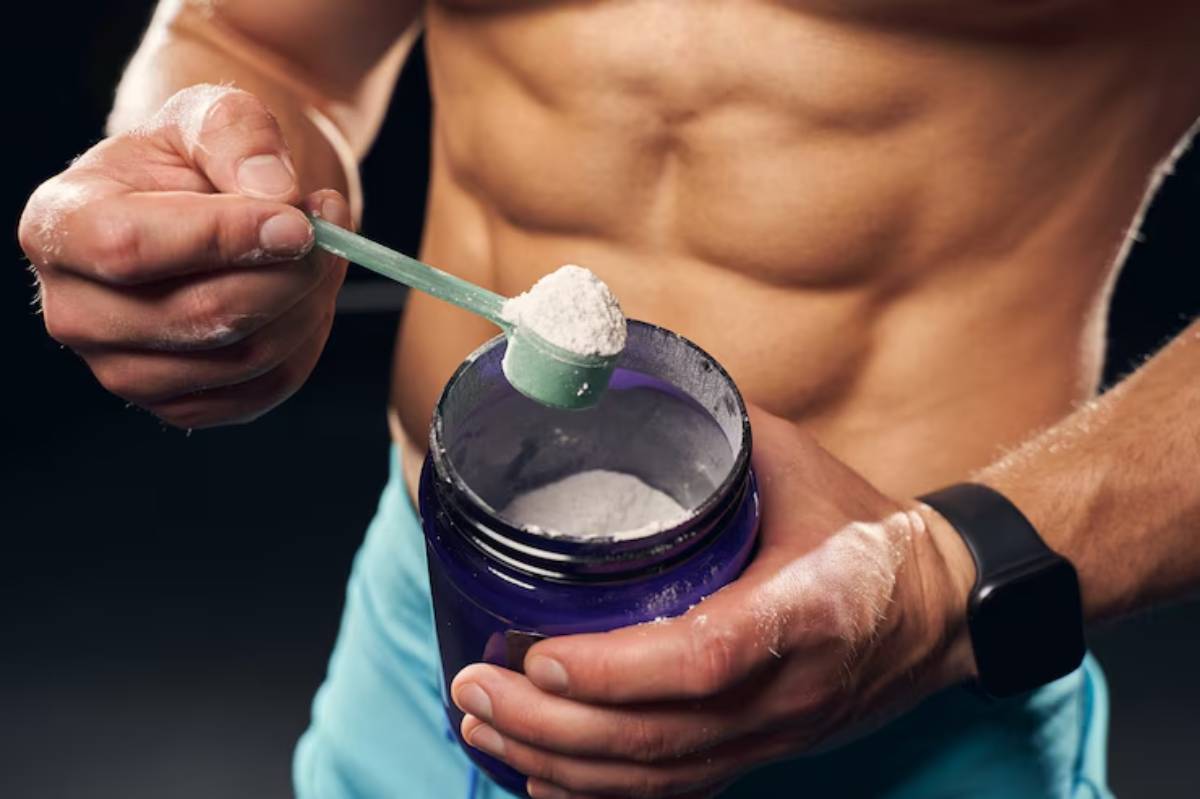A muscular man holds a green scoop of protein powder above a purple container, preparing for a workout.