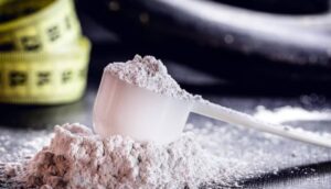 A white plastic scoop rests on a pile of powder, with a measuring tape blurred in the background, reflecting fitness themes.