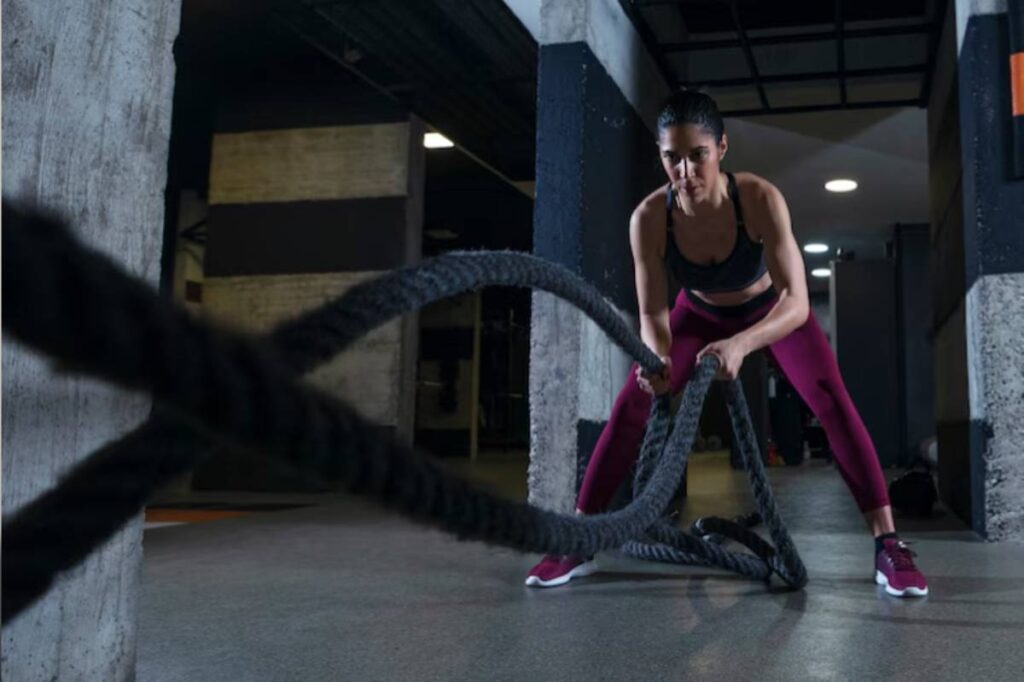 A person wearing workout clothes uses battle ropes, demonstrating strength and focus in a gym environment.