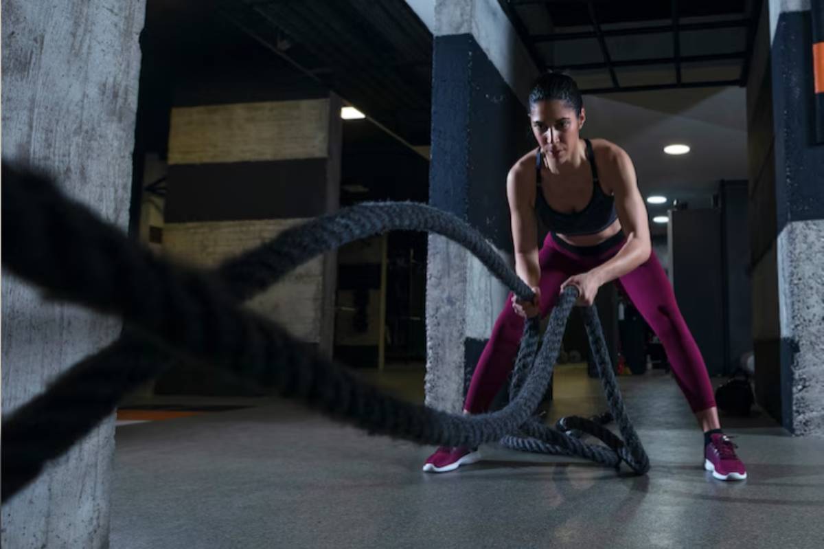 A person wearing workout clothes uses battle ropes, demonstrating strength and focus in a gym environment.