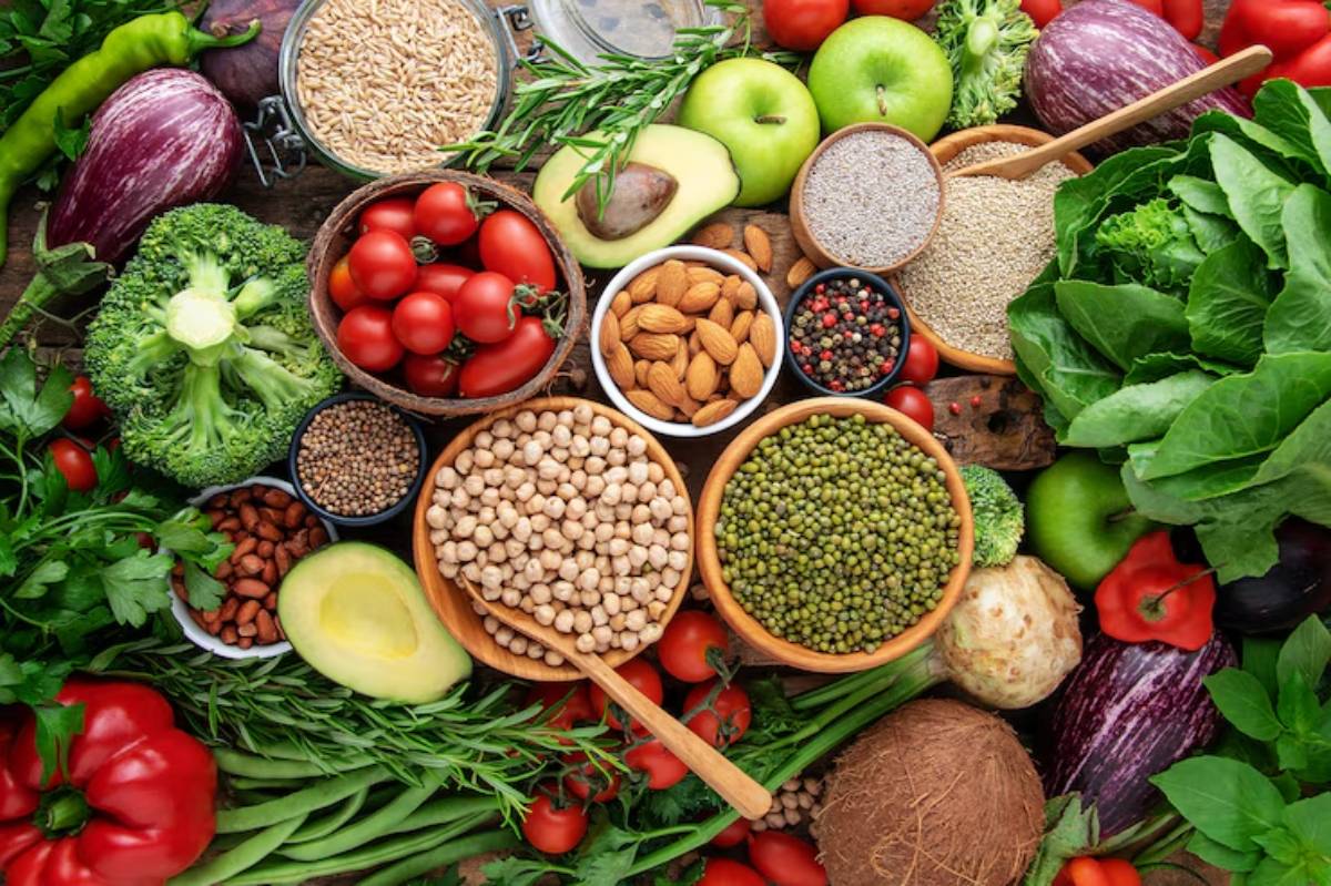 An assortment of fresh vegetables, fruits, and nuts arranged on a wooden surface, showcasing vibrant colors and healthy ingredients.